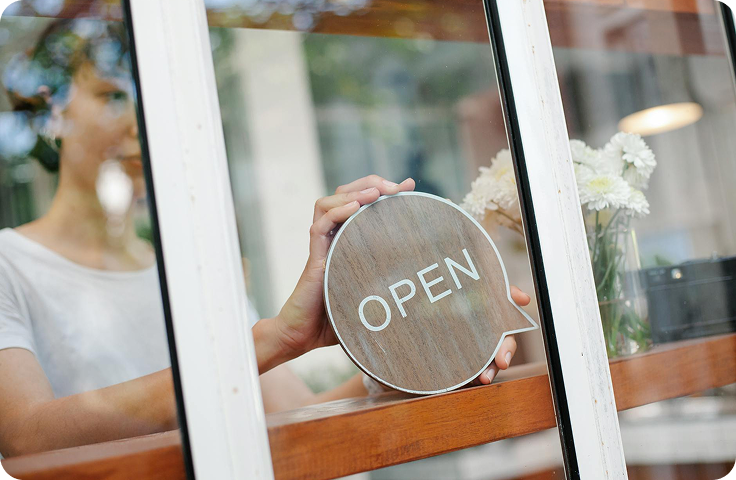 Small business owner hanging open sign on retail storefront window welcoming customers